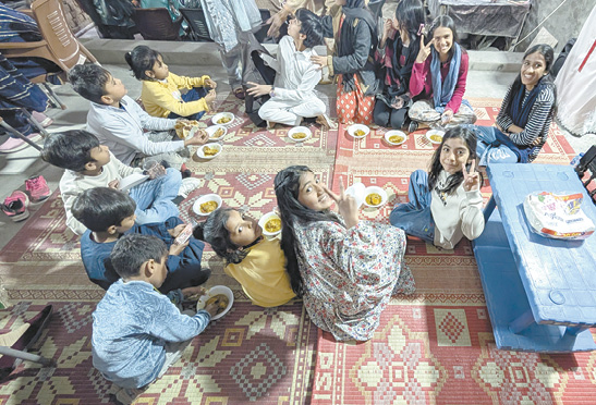 A group of people, including children, are sitting on a rug in a room. They are eating food and drinking from cups. There is a blue table in the room.

AI generated content